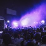 Grande público acompanha um show noturno diante de um palco iluminado com luzes coloridas.
