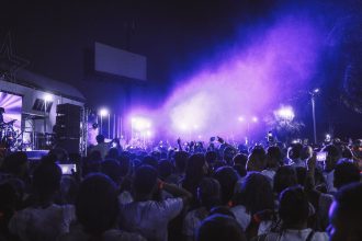 Grande público acompanha um show noturno diante de um palco iluminado com luzes coloridas.