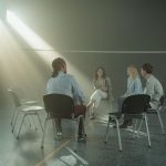 Grupo diverso de adultos participa de uma reunião de apoio em um ginásio iluminado.