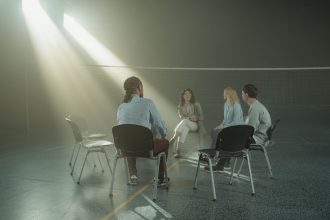 Grupo diverso de adultos participa de uma reunião de apoio em um ginásio iluminado.