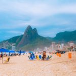 Frequentadores aproveitam a praia de Ipanema, com montanhas do Rio de Janeiro ao fundo.