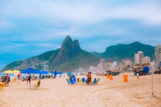 Frequentadores aproveitam a praia de Ipanema, com montanhas do Rio de Janeiro ao fundo.
