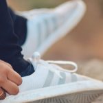 Close-up de uma pessoa amarrando um tênis Adidas ao ar livre.