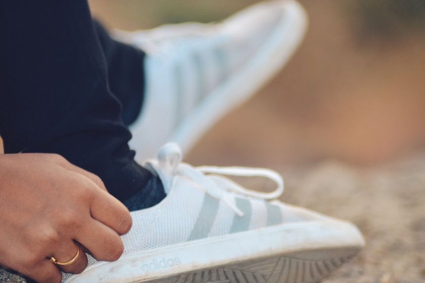 Close-up de uma pessoa amarrando um tênis Adidas ao ar livre.